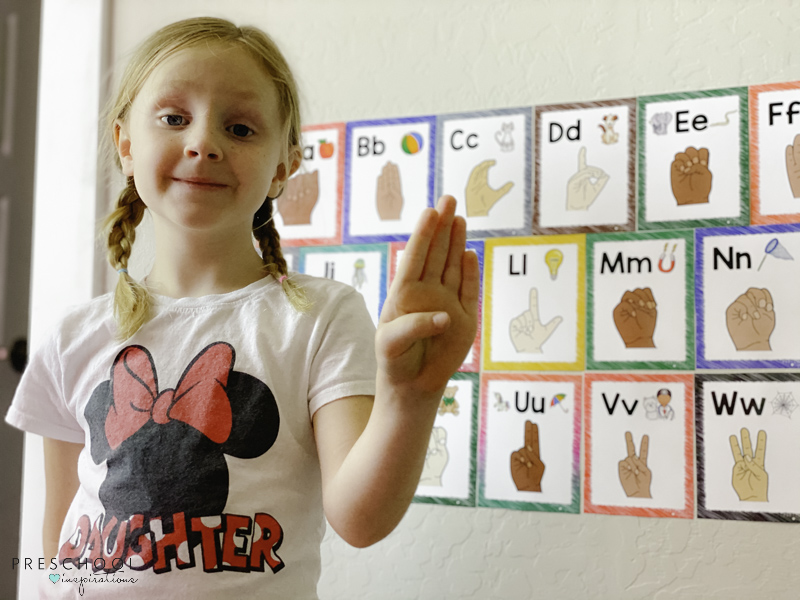 young girl proudly holding up the letter B in ASL