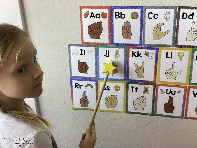 a young girl using a pointer with ASL alphabet wall cards