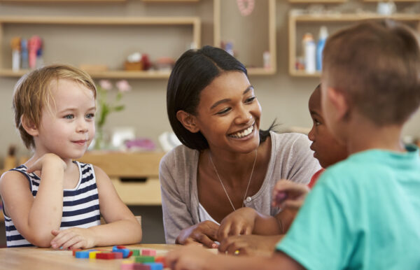 A smiling teacher talks to her preschool class at a table