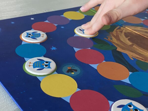 a child's hand playing the board game hoot owl hoot