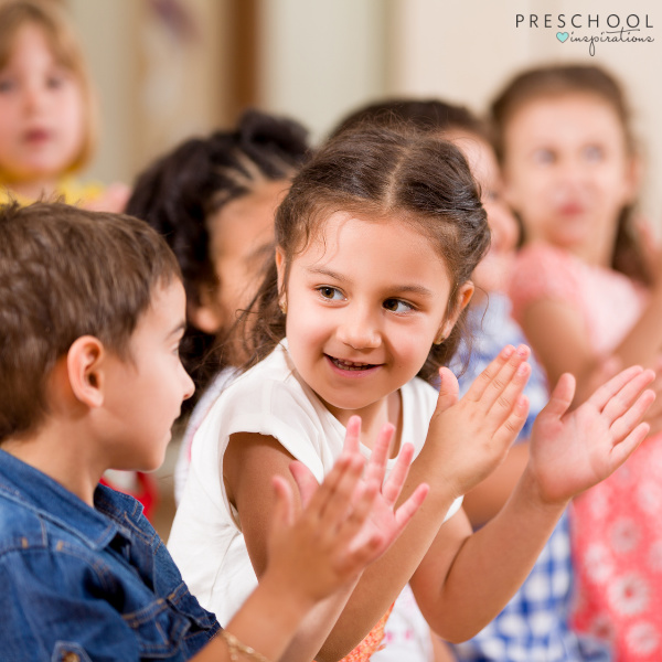two preschoolers smile and clap during a preschool circle time